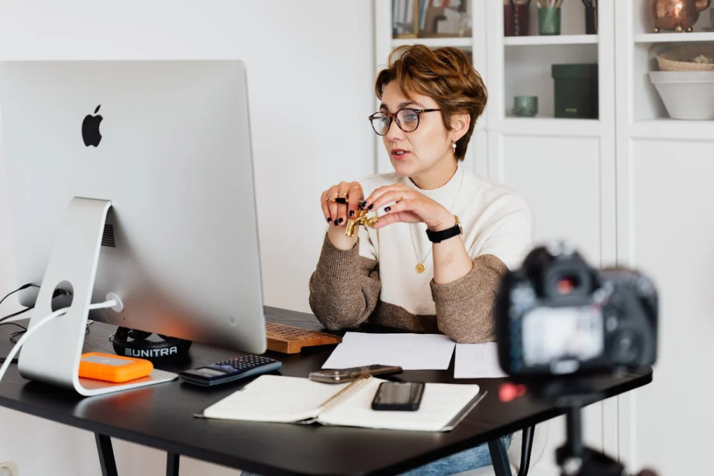 Den perfekten Tutor finden: Ein umfassender Leitfaden für Lernende in Deutschland 2 Das Bild zeigt eine Person, die an einem Schreibtisch mit einem iMac-Computer, einem Notizbuch und anderen Büromaterialien sitzt. Das Gesicht der Person ist zur Wahrung der Privatsphäre pixelig dargestellt. Vor der Person befindet sich eine DSLR-Kamera auf einem Stativ, was darauf hindeutet, dass die Person möglicherweise filmt oder streamt. Diese Einrichtung könnte relevant sein für Diskussionen über Home-Office, Online-Inhaltsproduktion oder Datenschutz in digitalen Medien.